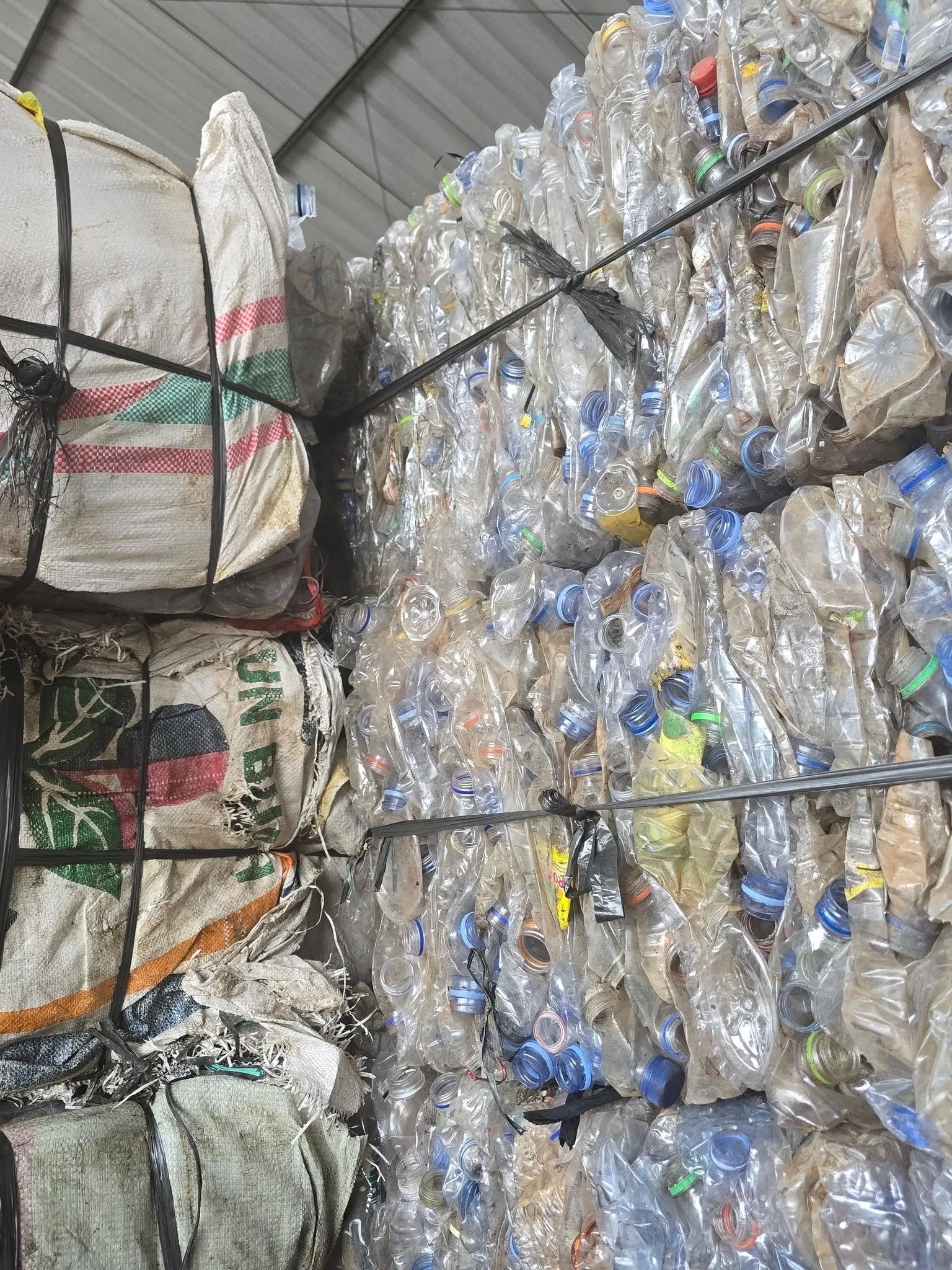 Tumpukan bal press material PET bening di fasilitas RRA Plastik